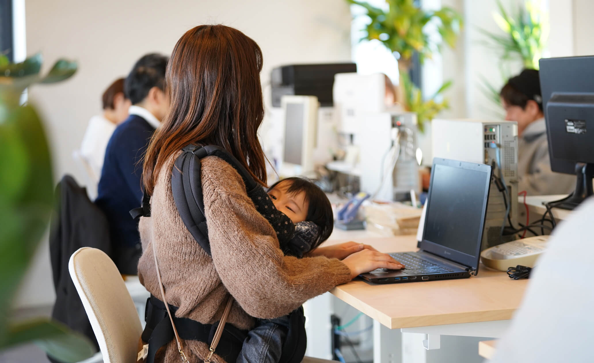 抱っこ紐で子供を抱っこしながらパソコンで作業をするスタッフの写真